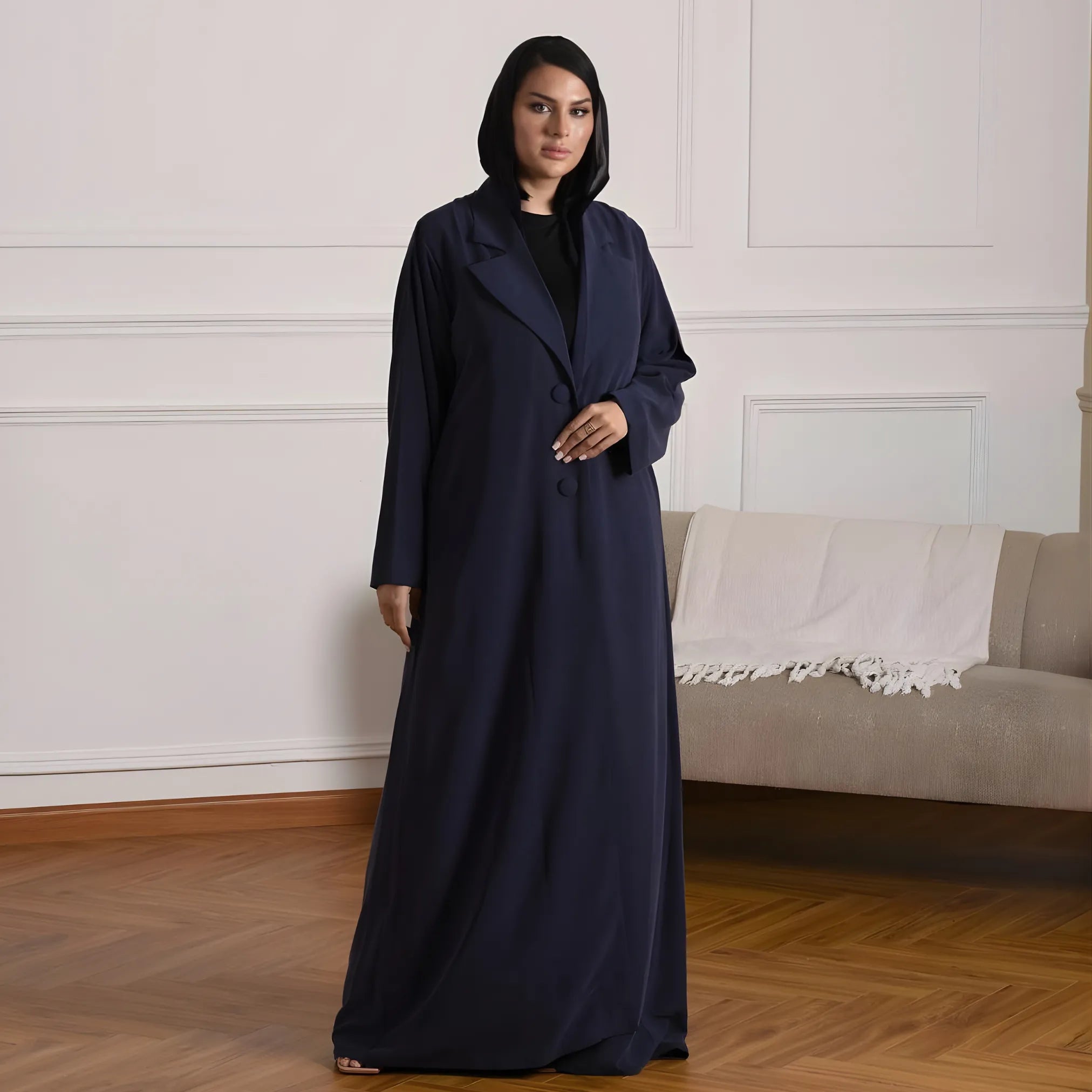 Woman wearing a long dark blue abaya in a room with a beige sofa.