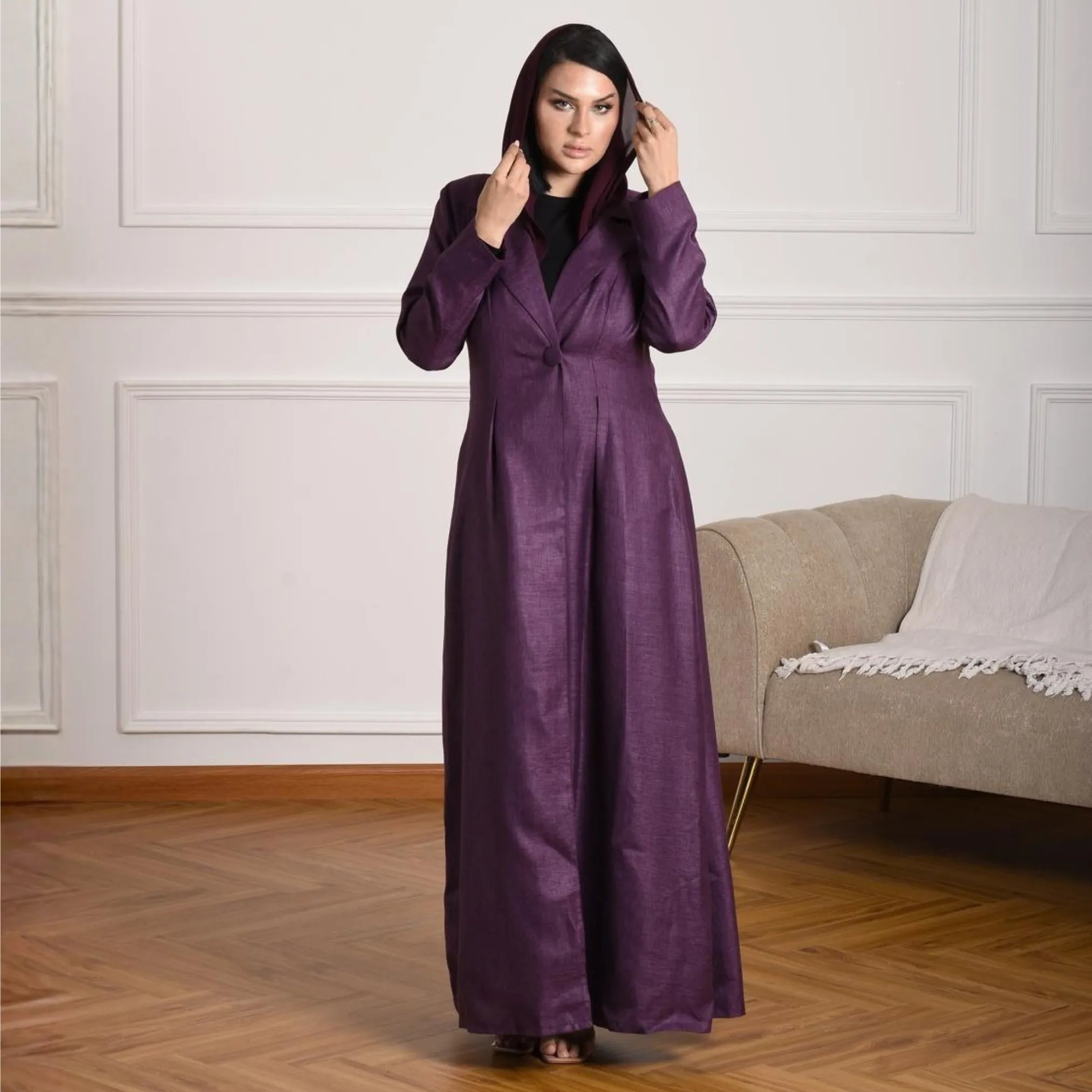 Woman wearing a long purple coat abaya in a room with a beige sofa.