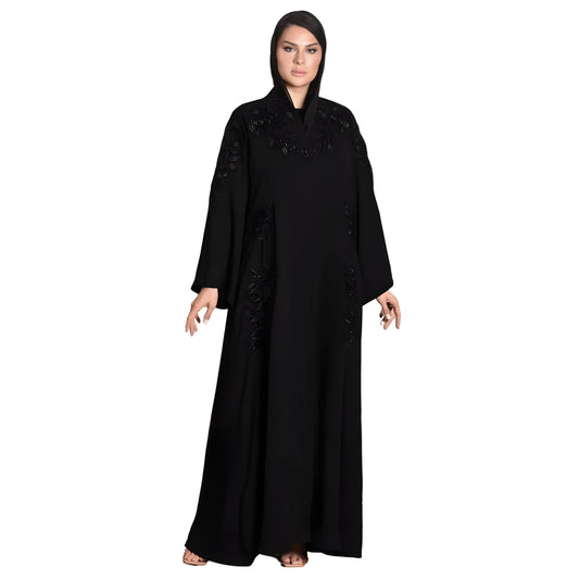 Woman wearing a black abaya with intricate detailing on a white background