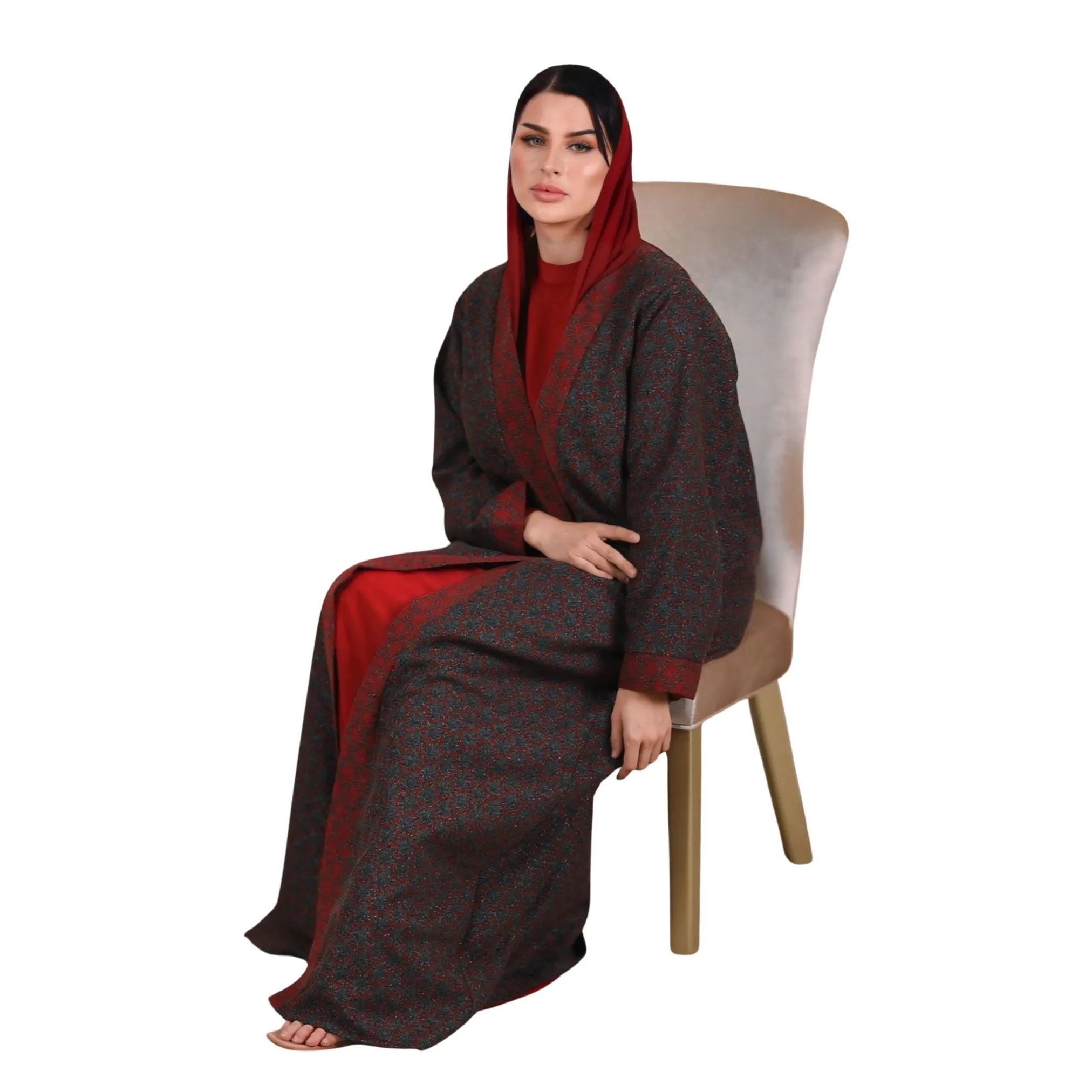 Woman wearing a long, dark brown and red abaya sitting on a chair against a white background