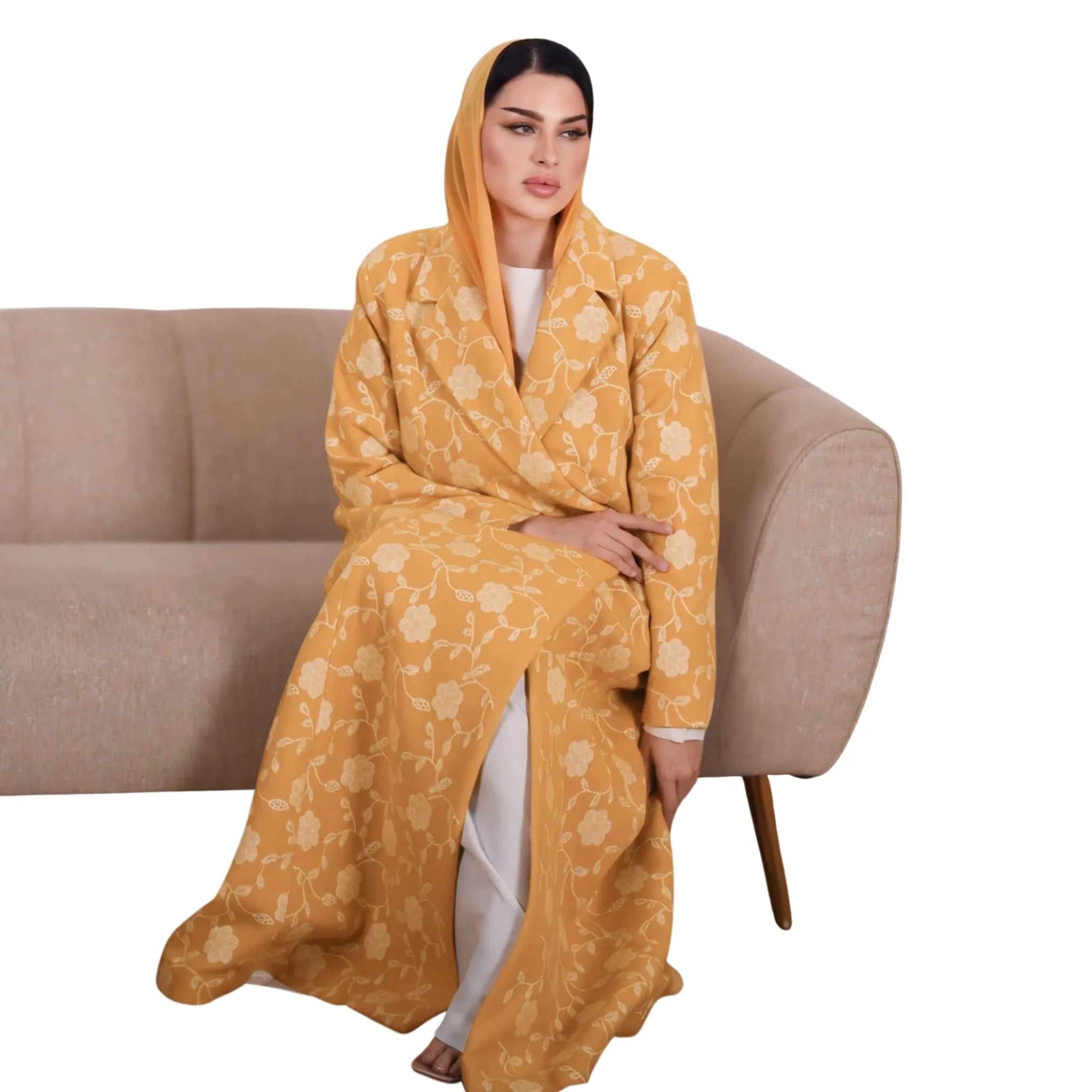 Woman sitting on a couch wearing a yellow floral Abaya.