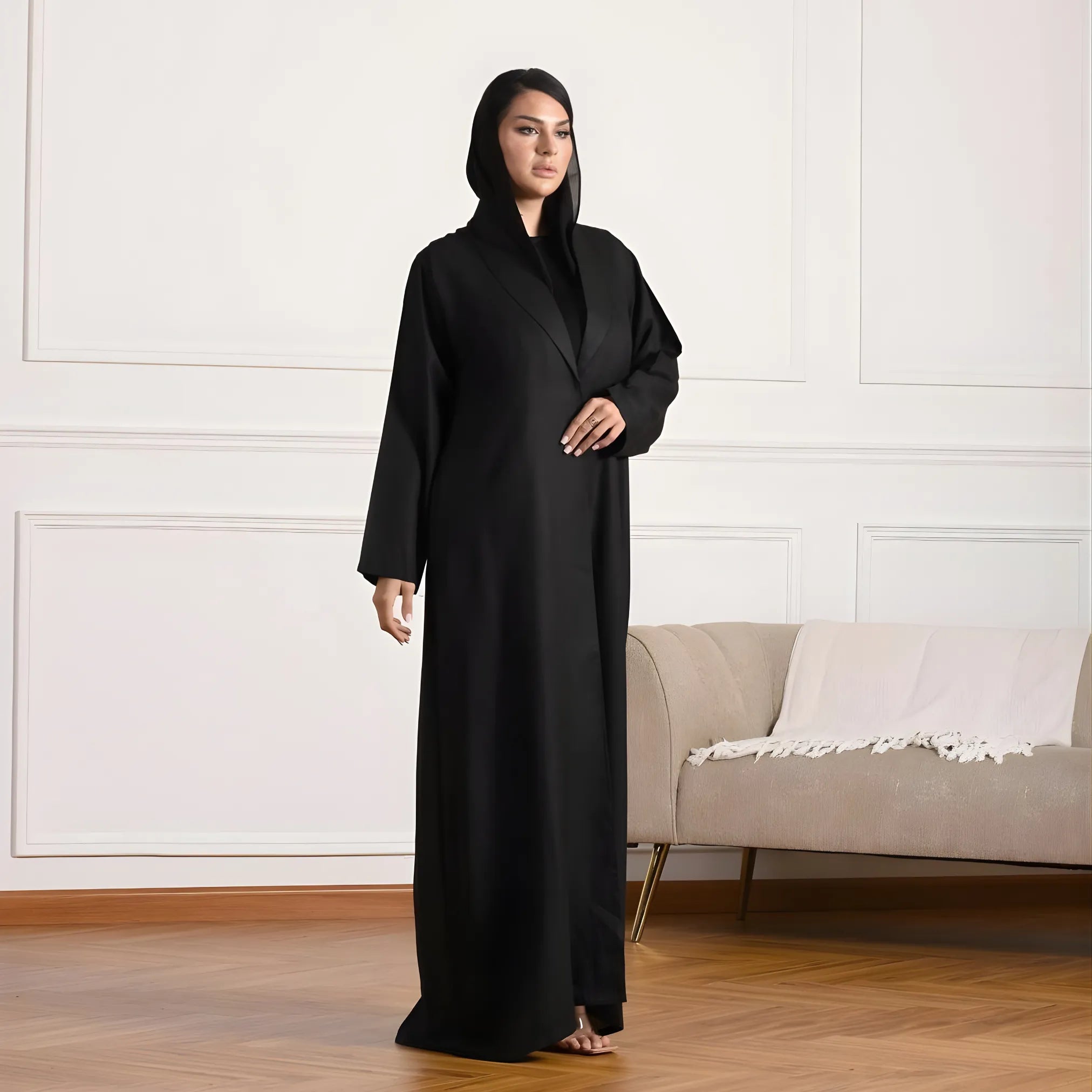 Woman wearing a black abaya in a room with a beige sofa and white walls.