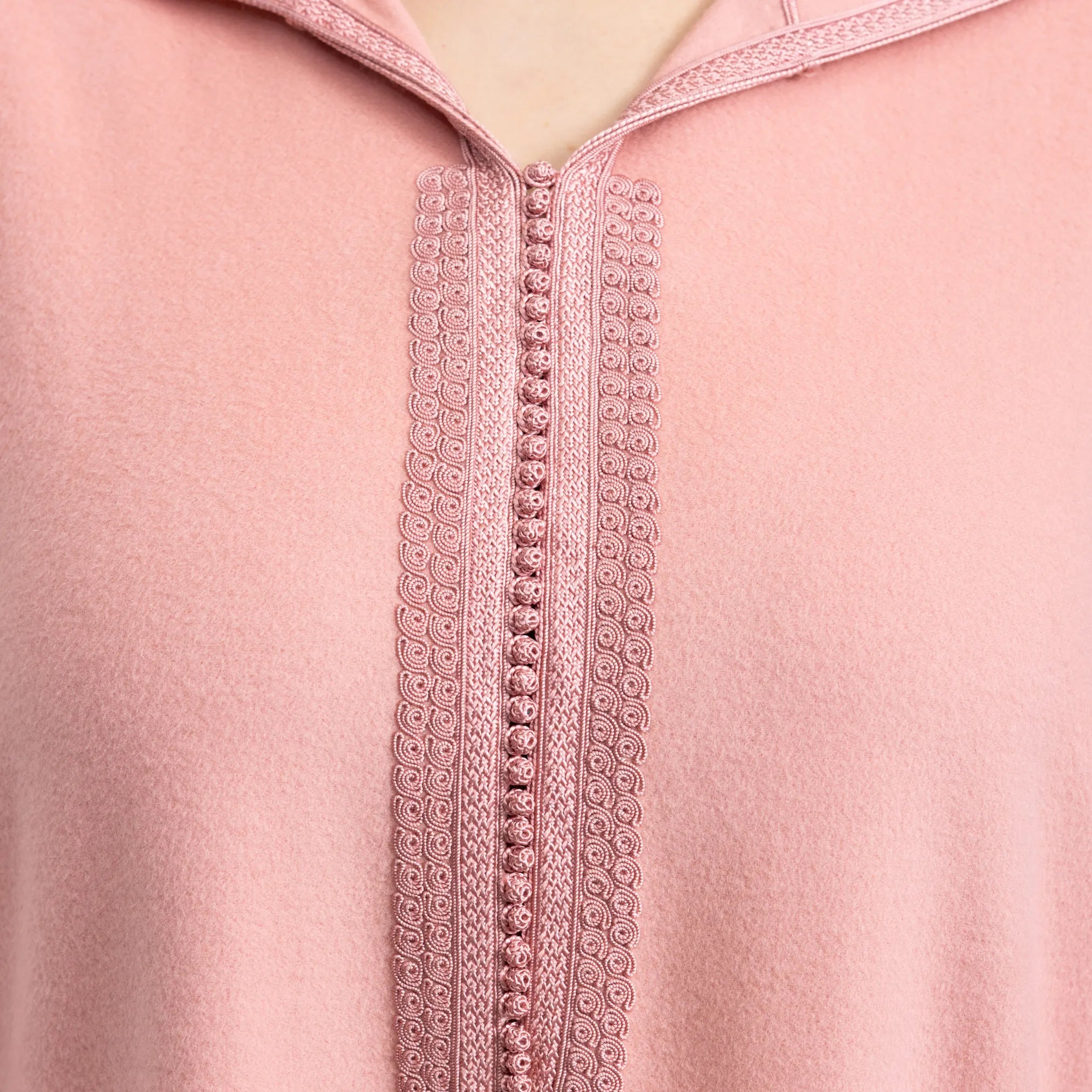 Close-up of a pink jalabiya with intricate lace detailing on a matching fabric background