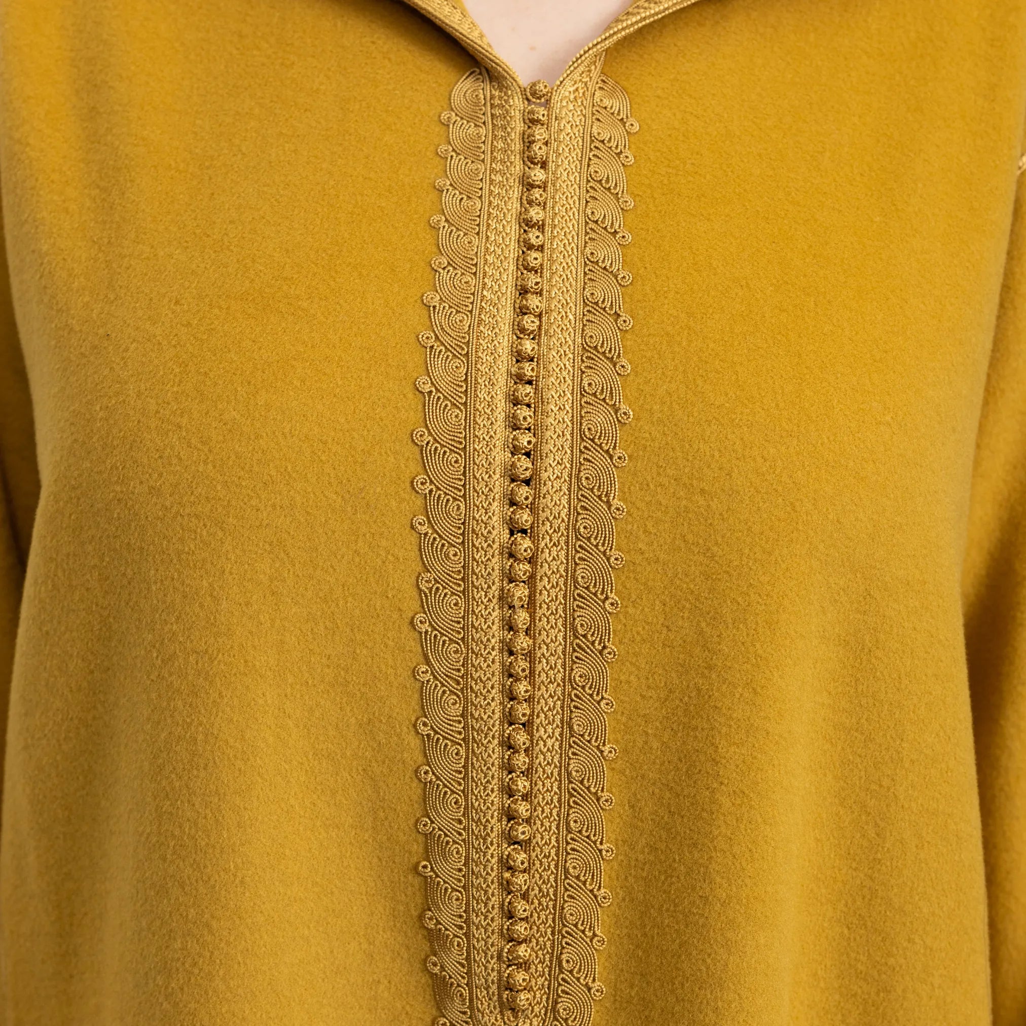 Mustard yellow jalabiya with intricate gold embroidery on a plain background