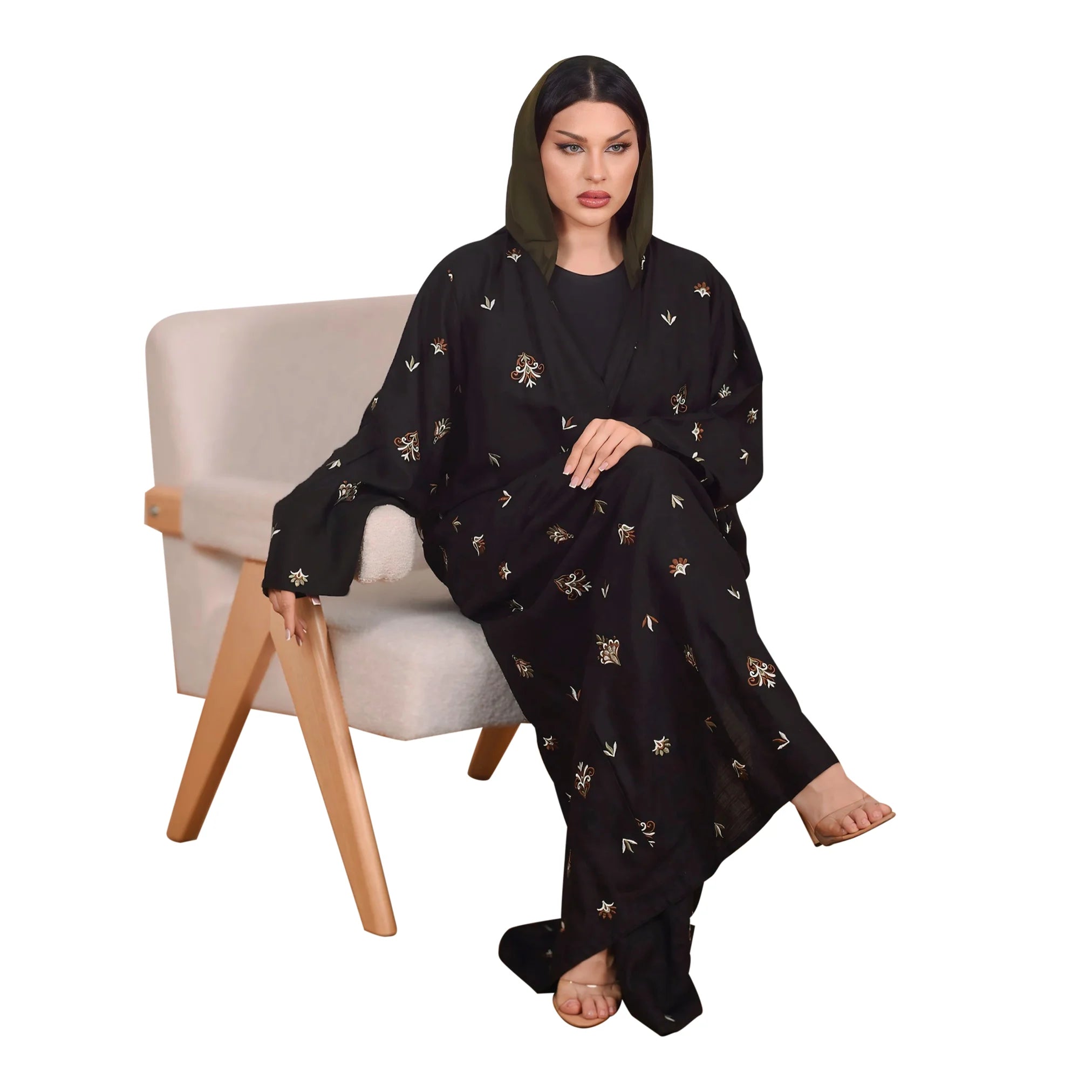 Woman wearing a black abaya with gold embroidery sitting on a chair against a white background