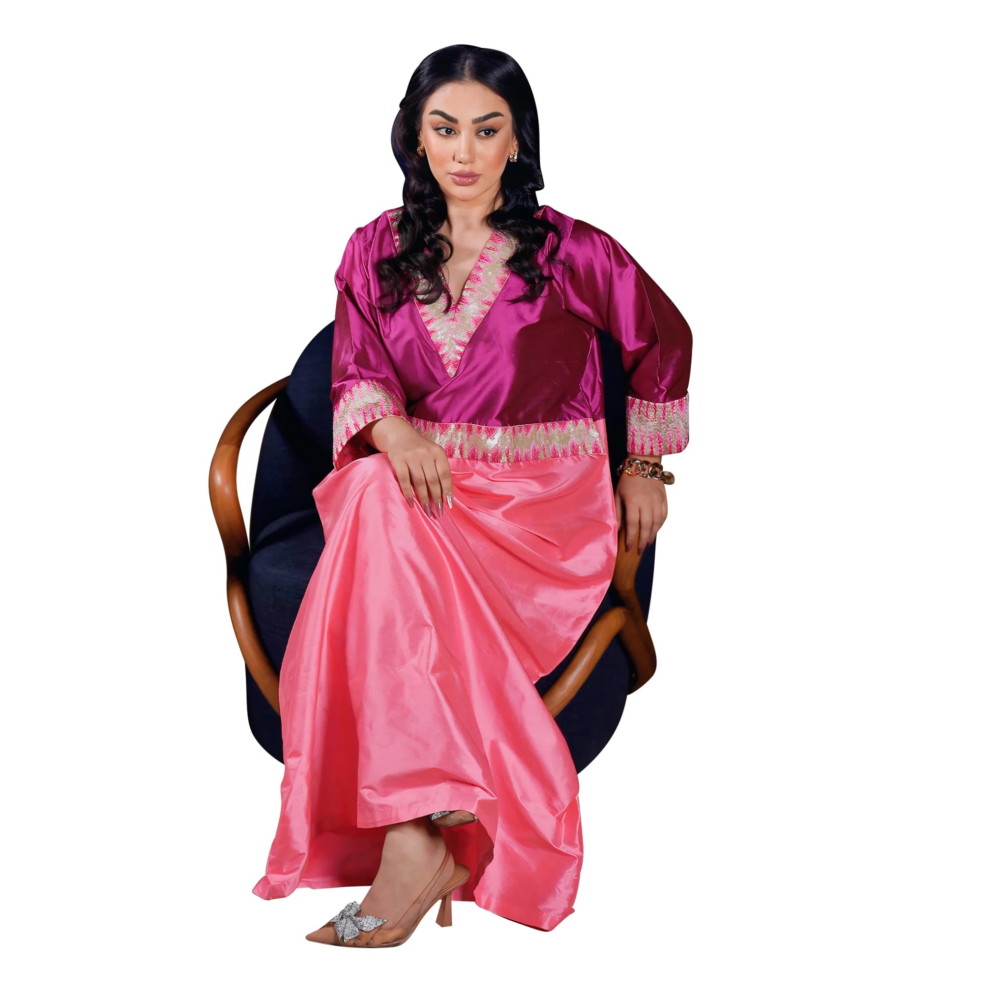 Woman wearing a pink and red traditional outfit sitting on a chair with a white background