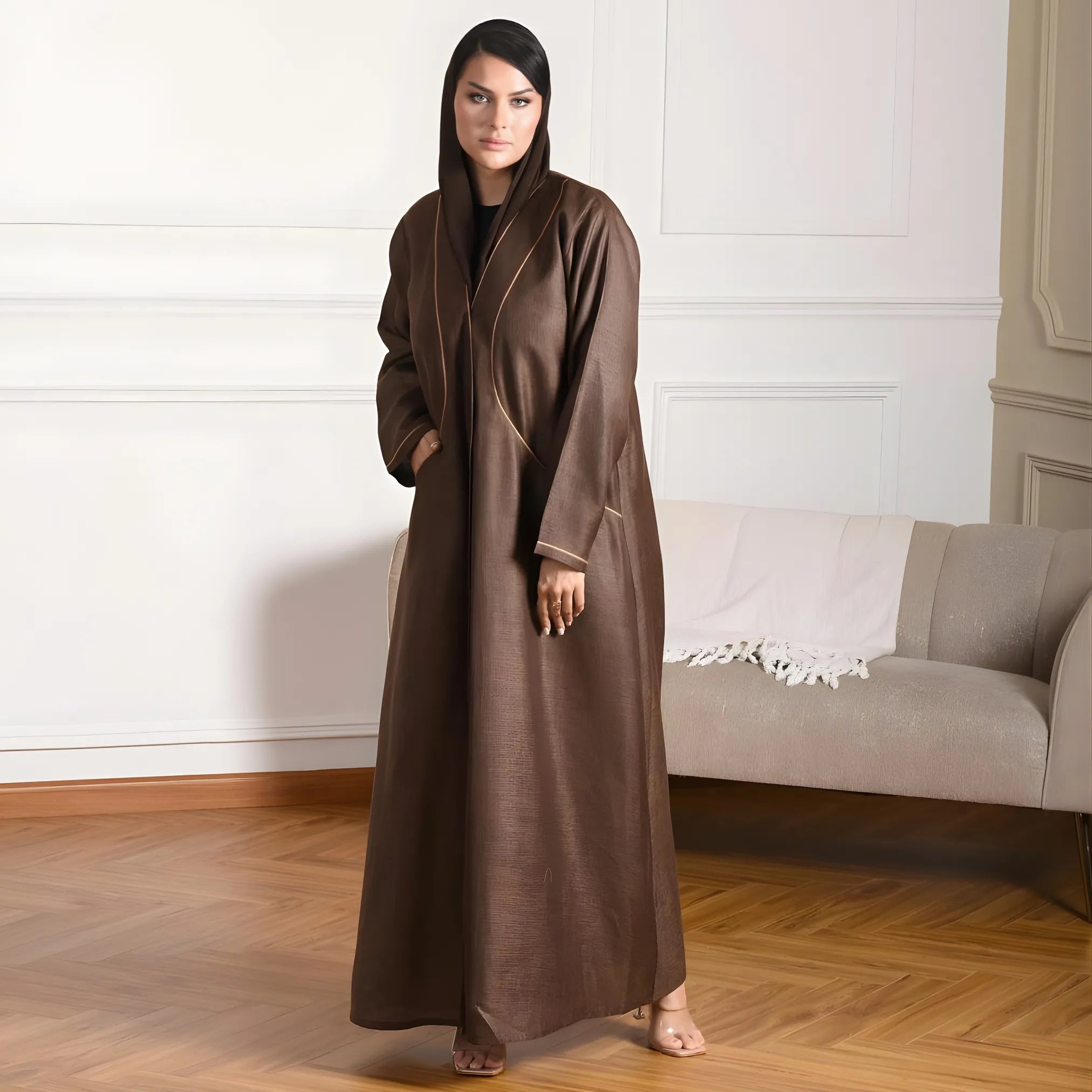 Woman wearing a choco brown abaya in a room with a sofa and white walls.