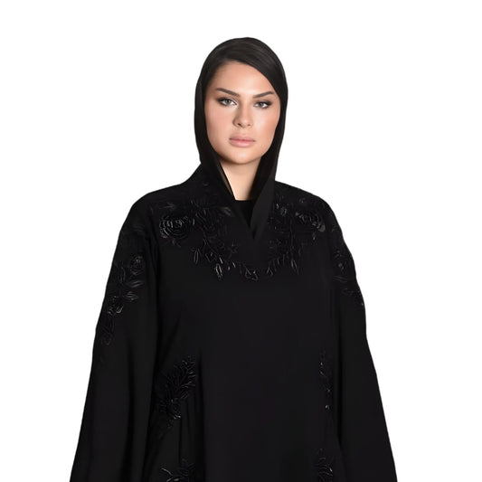 Woman wearing a black abaya with floral embroidery on a white background