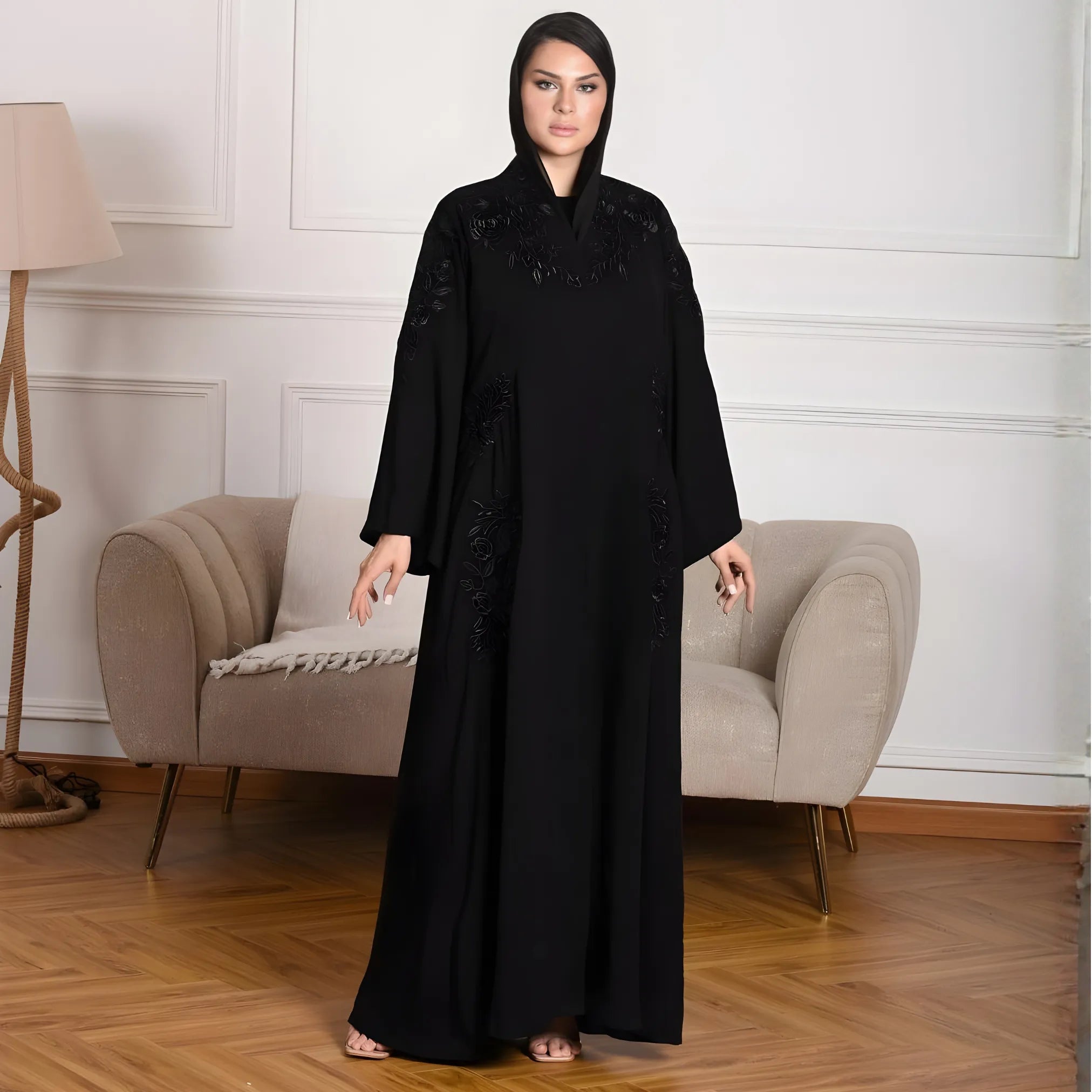 Woman wearing a black abaya in a room with a beige armchair and lamp.