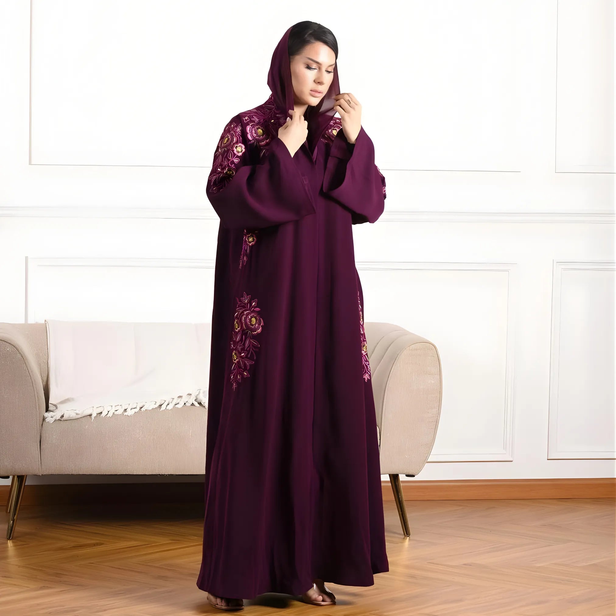 Woman wearing a long, dark purple Abaya with floral embroidery in a room with a beige sofa.