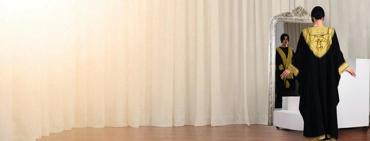 Women wearing a black and gold outfit standing in front of a mirror with a white curtain background