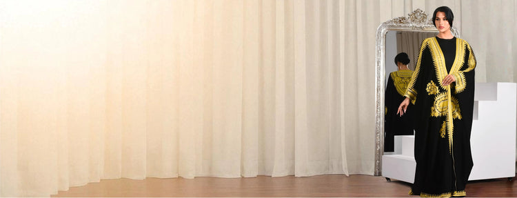 Woman in a black and gold dress standing in front of a mirror with white curtains.