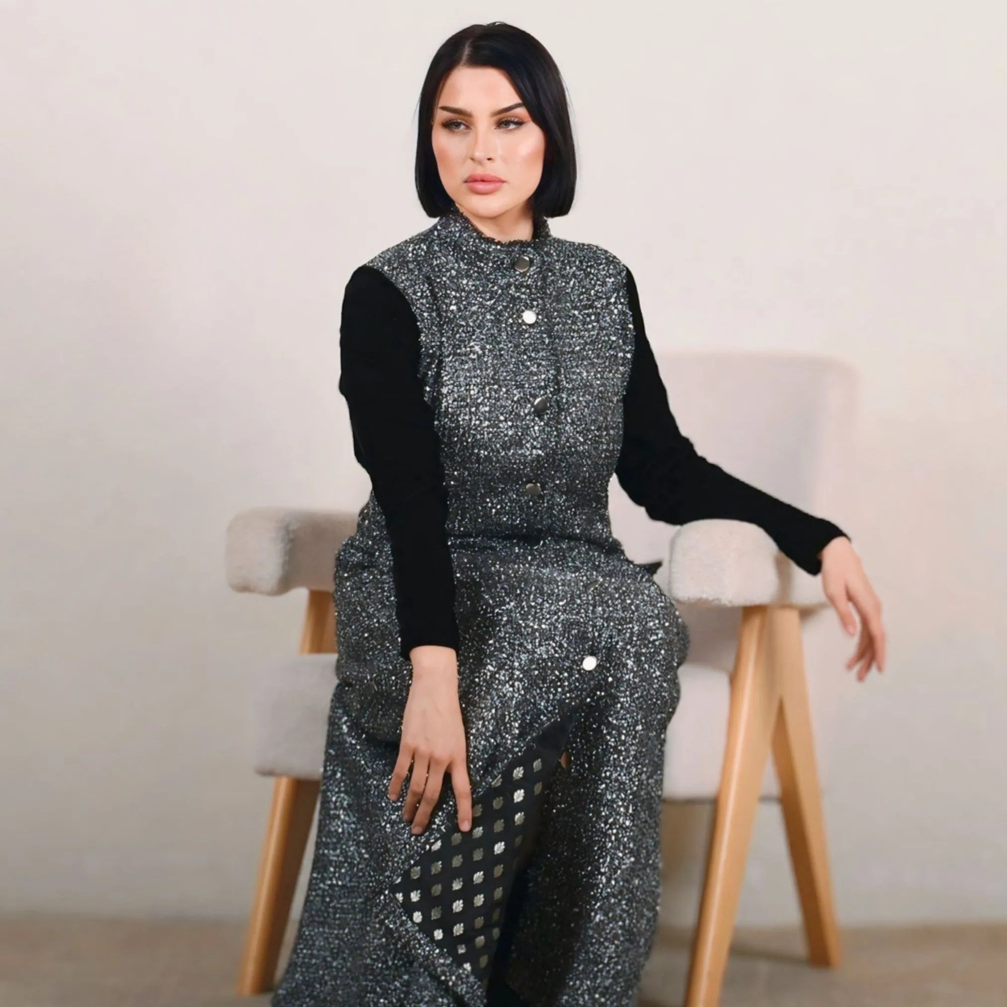 Woman wearing a sparkly silver outfit with a black top in a minimalistic setting.