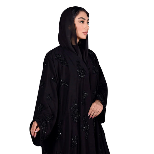 Woman wearing a black abaya with intricate designs on a white background