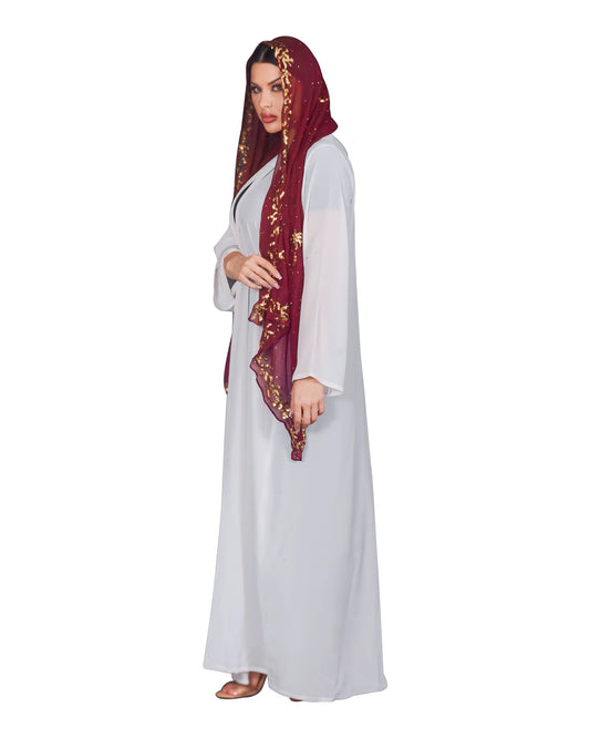Woman wearing a white dress abaya and a maroon hijab with gold embroidery on a white background 
